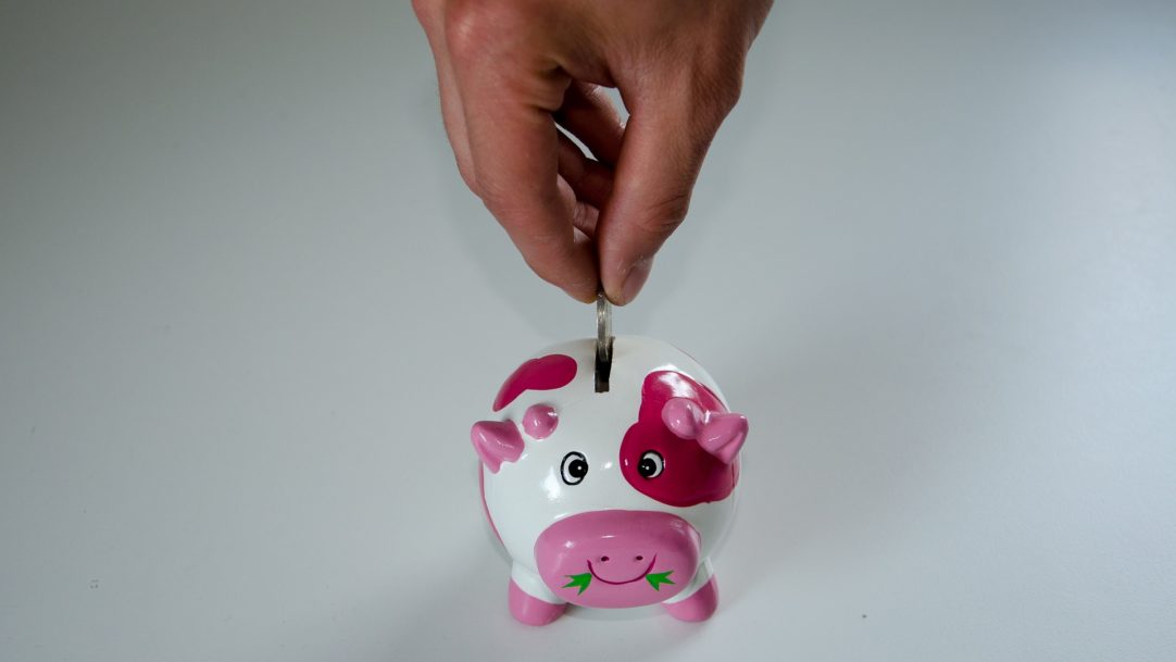 Hand inserting coin into a piggy bank